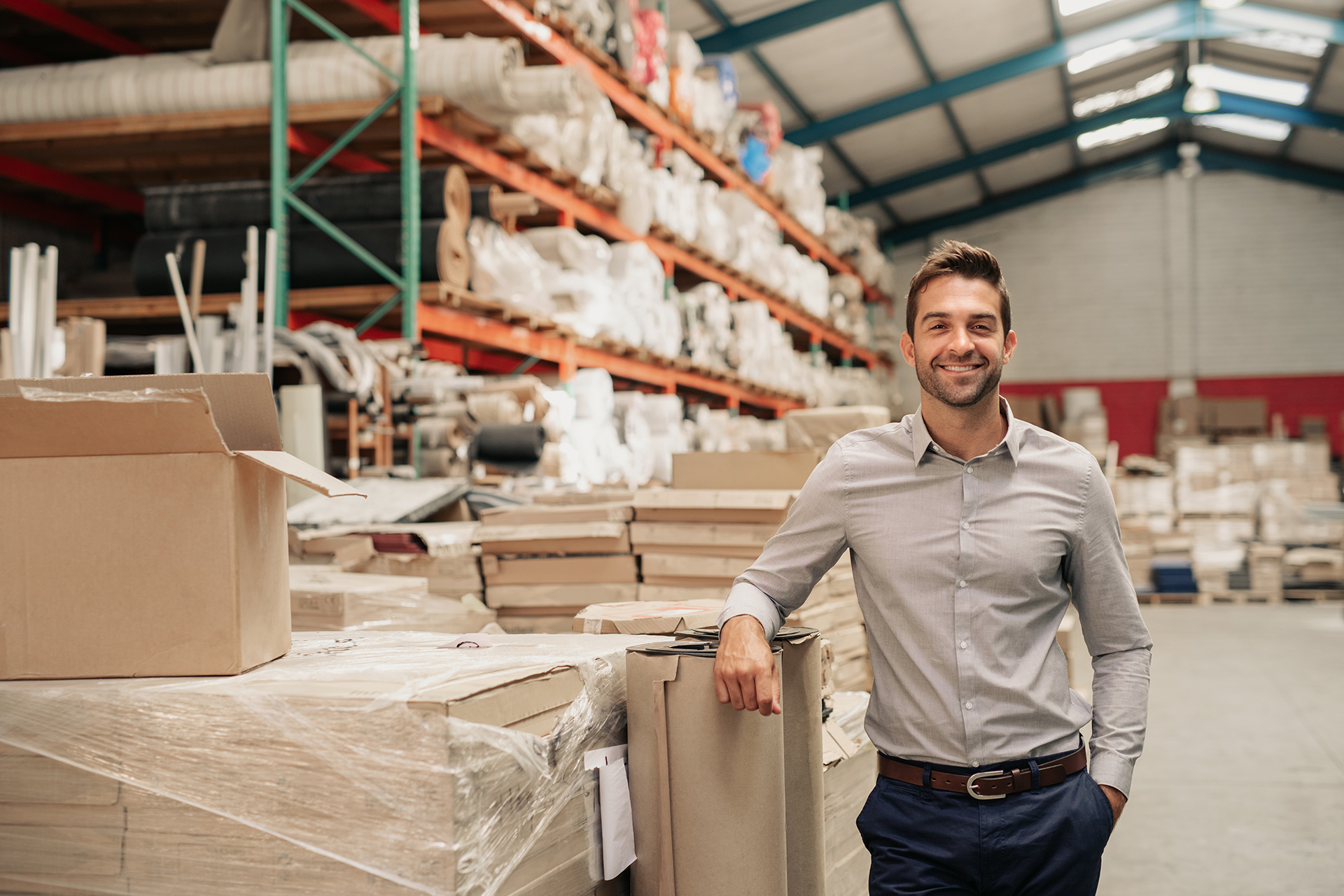 Man smiling while leaning against cardboard boxes in a large warehouse